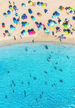 Aerial drone view of colorful umbrellas on sandy beach, swimming people in blue sea on sunny summer day. Top down view. Mallorca, Balearic Islands, Spain. Tropical. Clear turquoise water. Travel