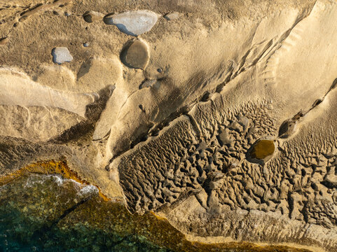 Aerial view of golden sandstone formations etched by time and tide meet the turquoise sea, Gozo, Malta.