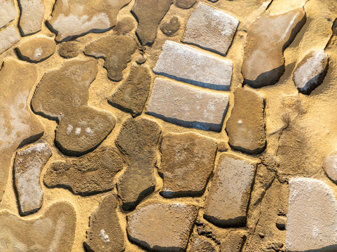 Aerial view of an abstract mosaic of irregular rock pieces in a sandy setting, creating a textured, earthy pattern, Malta.