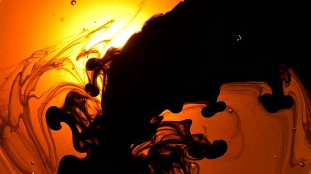 Crude oil spill dissolves in water creating a dark abstract shape or Black liquid merges with amber liquid in an abstract pattern