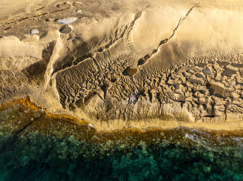 Aerial view of the sculpted Qolla I-Bajda Salt Pans meeting the turquoise sea, Iz-Zebbug, Gozo, Malta.