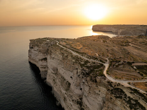 Aerial view of rugged cliffs meet the azure sea under a golden sunset sky at Sanap Cliffs, Munxar, Gozo, Malta.