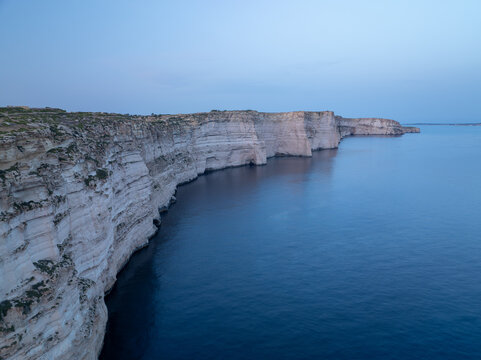 Aerial view of the rugged Sanap Cliffs plunging into the deep blue sea under the fading twilight, Munxar, Gozo, Malta.