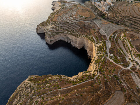 Aerial view of rugged cliffs plunging into the deep blue sea, where the terraced landscape meets the coastal edge, Munxar, Gozo, Malta.