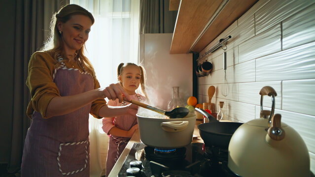 Friendly family cooking soup at kitchen closeup. Loving mother teaching daughter