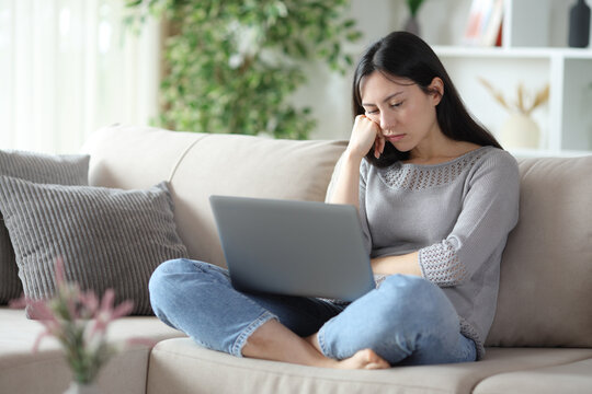 Bored asian woman checking laptop on a couch