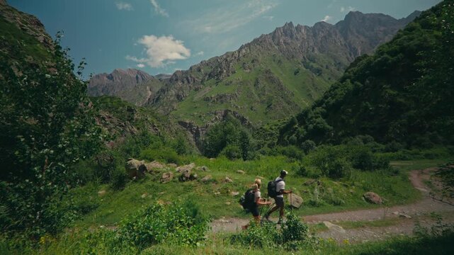 Two people hiking on a gravel path with the Caucasus mountains in the backdrop, featuring towering granite peaks in Georgia and capturing adventure, nature, and scenic exploration.