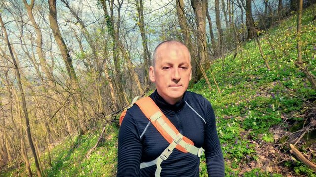 Authentic mature man walking through a blooming spring woodland path with purple flowers. Promoting personal health, fitness, mental well-being, and the calming power of nature for stress relief.