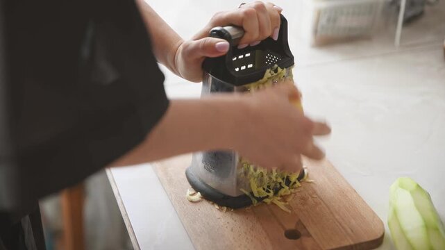 Hands grating potato on wooden cutting board in bright kitchen with natural light