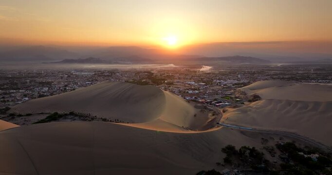 Touristic Huacachina desert oasis and dunes in Peru at sunset, aerial pullback