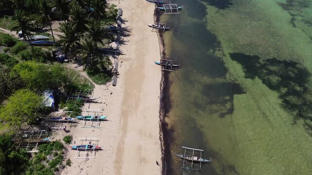 Aerial view of traditional Bangka boats anchored along a tropical shoreline with clear water and sandy beach surrounded by lush green vegetation on Bantayan Island Philippines Southeast Asia
