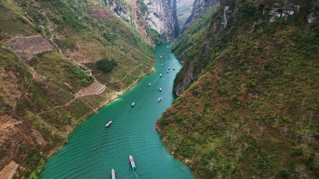 Aerial drone footage of Nho Que River flowing through Tu San Canyon with towering limestone cliffs turquoise water small boats and a deep mountain gorge in northern Vietnam