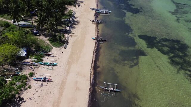Aerial view of a tropical beach lined with palm trees and clear turquoise water with traditional Bangka boats creating a vibrant coastal scene on Bantayan Island Philippines Southeast Asia