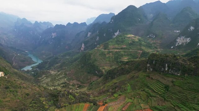 Drone view of steep hillside agriculture with terraced fields overlooking a narrow mountain valley and a winding river flowing through isolated highland terrain in Ha Giang Province.
