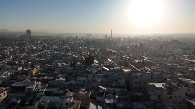 Atmospheric aerial drone shot of Damascus at sunset, featuring a hazy urban horizon and traditional minarets