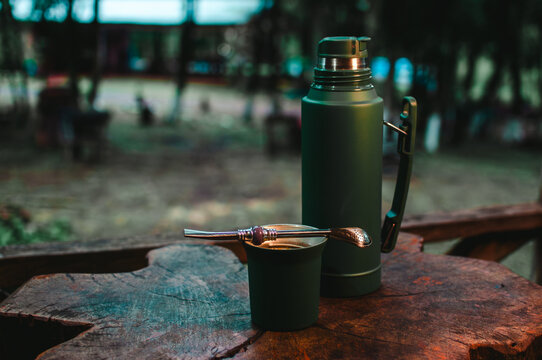 mate y termo de acero color verde &iacute;ndigo sobre una mesa de madera r&uacute;stica frente a la casa, d&iacute;a de relajaci&oacute;n en la selva