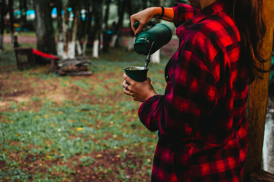Mujer con camisa a cuadros cebando mate en la naturaleza