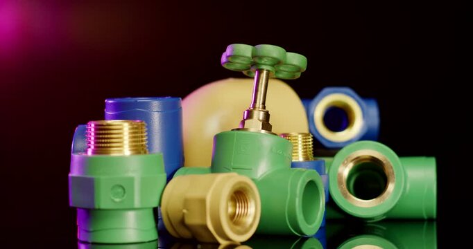 Close up of various colorful plastic and brass industrial plumbing fittings and valve on a black background