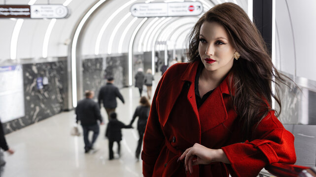 A beautiful brunette in a red coat standing at a subway station, city rhythm
