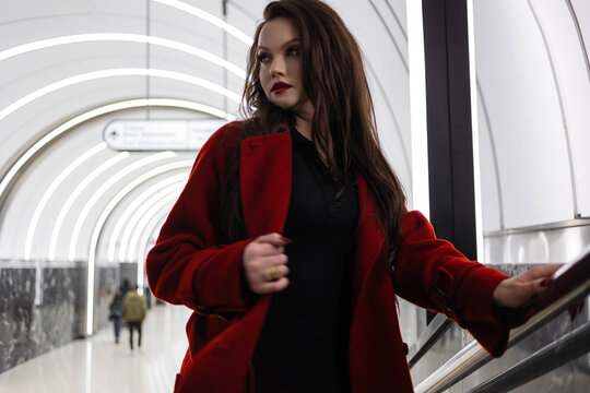 A stylish brunette in a red coat rushing on a subway platform, city life