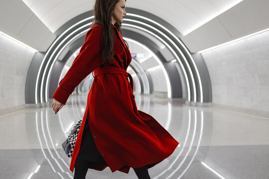 A young brunette in a crimson coat hurrying with a handbag through a subway concourse