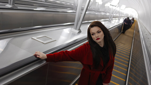 A young dark-haired woman in stylish clothes going up on an escalator from the subway