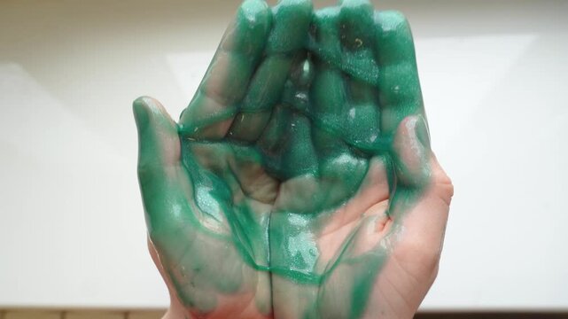 A green stringy slime with sequins in the hands of a child