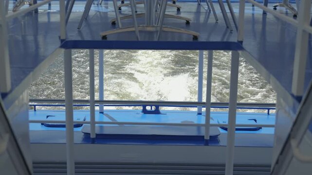 Abstract geometric view from the stern of a boat. The blue grey deck frames the churning white wake of the vessel as it moves through the water. A calm, tranquil scene of travel transportation