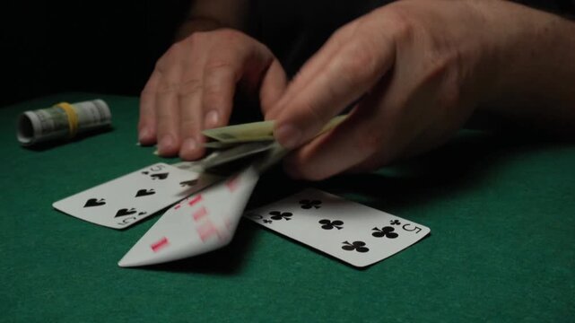 The player's hands take money from the winning playing cards and the green felt table, demonstrating the intensity of the card game in low light conditions, focusing attention on the excitement