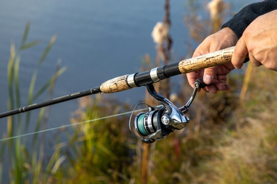 Hand holding fishing rod with spinning reel, angling gear by freshwater lake