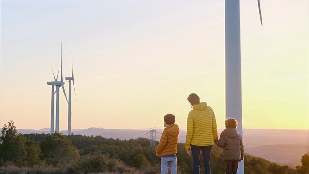 Family observing large wind turbines on a hill at sunset, symbolizing a commitment to clean energy and environmental sustainability for future generations