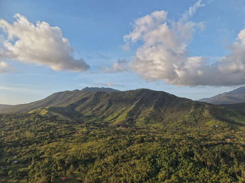 Aerial drone view reveals Mount Ari green slopes bathed in warm afternoon sunlight with dense tropical vegetation covering rolling hills and scattered rural structures in Bakungan district Palawan