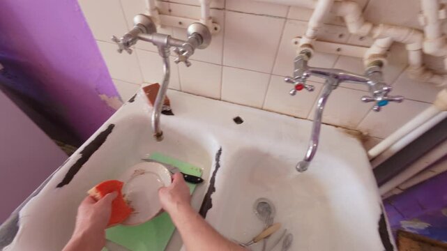 The guy washes dirty dishes, plates and spoons with water. The man deftly moves the sponge over the plate.  The process of washing dishes in the dishwasher sink. From the first person.