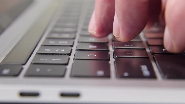 Low angle, extreme close-up of hands typing on a laptop. Focus on the mechanical movement of keys with a shallow depth of field. Modern office, programming, and remote work concept.