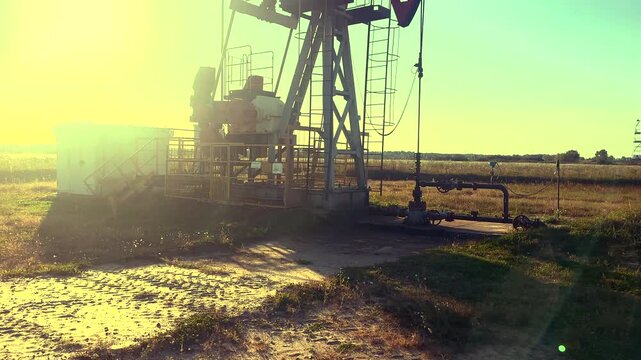 Crude pump jack on sunrise in oil field. Oil Pump Jack Operates on Beautiful Sunset at Oil Field in Industrial Area. Oil drill rig, drilling derrick in oilfield. Crude petroleum industry. 