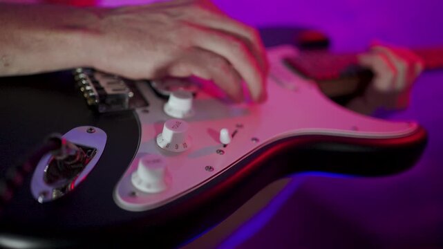 Close-up of Musician Playing Electric Guitar on Stage. Guitarist hand strumming strings on a black electric guitar. Professional musician performing under atmospheric red stage lights.