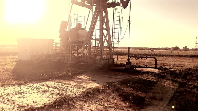 Crude pump jack on sunrise in oil field. Oil Pump Jack Operates on Beautiful Sunset at Oil Field in Industrial Area. Oil drill rig, drilling derrick in oilfield. Crude petroleum industry. 