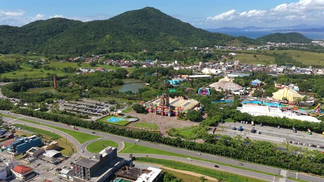 Drone establishing view of Beto Carrero World in Penha, Santa Catarina, Brazil, showing amusement park, parking, roads and forested hills in wide landscape.