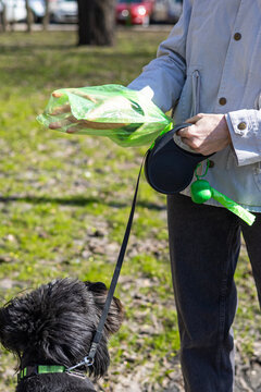 Woman using public dog waste station with poop bag dispenser outdoors, responsible pet care, hygiene practice, urban service, cleanliness.