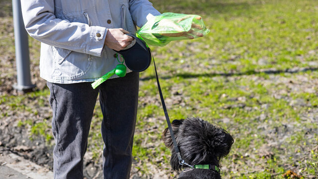 Woman using poop bag dispenser outdoors, responsible pet care, hygiene practice, urban service, cleanliness.