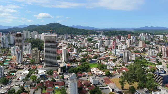 Drone establishing view of Joinville, Santa Catarina, Brazil, with dense downtown skyline, high-rise buildings under construction and Serra do Mar mountains.