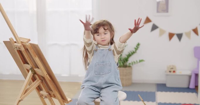Preschooler asian daughter waves paint stained fingers after fingerpaint session, creativity and imagination growing, home schooling activity for family, bonding love care, weekend learning indoors