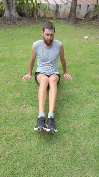 Bearded Man Doing Russian Twist Core Exercise on Green Grass in Tropical Garden