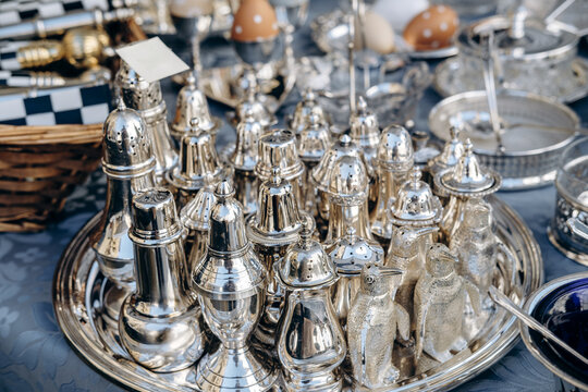 An elegant arrangement of vintage silver tableware and ornate tea set pieces displayed on a patterned blue tablecloth, featuring crystal bowls, polished serving trays, spoons 