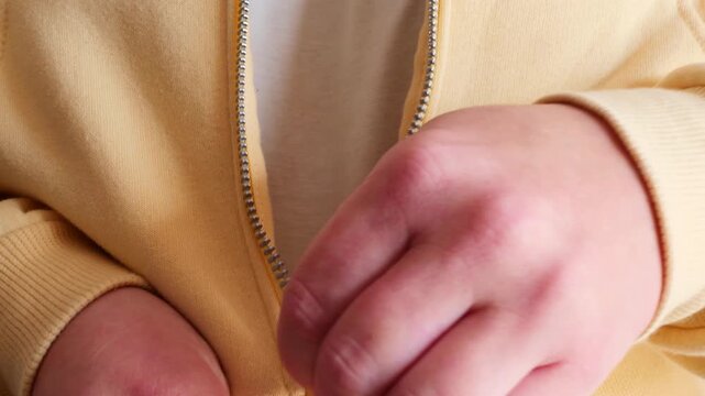 close up of hands closing zipper on yellow sweatshirt. action expresses comfort, coziness, starting the day. concept of self care, everyday life, autumn mood, casual wear promotion, lifestyle media