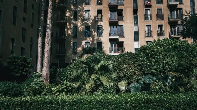 Lush greenery surrounds a large apartment building with many windows and balconies.