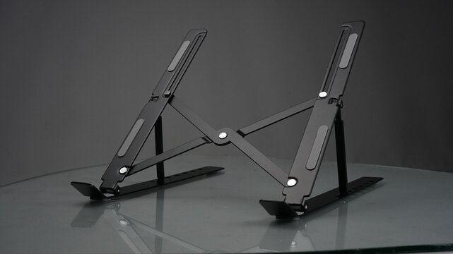 Black foldable laptop stand on reflective gray surface