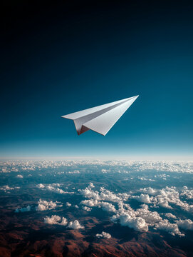 A white paper airplane flying over the horizon with thick white clouds and mountain ranges on the ground asa concept of safe flying and travelling