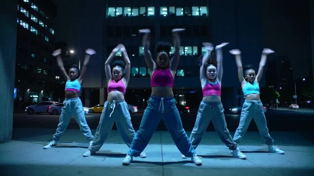 Starting on beat, five dancers performing hip moves on sidewalk, shifting, ending squat, crop tops