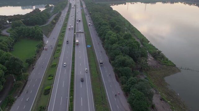 Closer aerial perspective of Ring Road 3 traffic flow in Hanoi with cars and trucks moving along divided lanes beside water and greenery